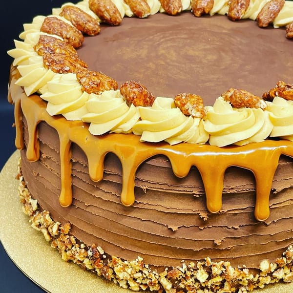 Chocolate cake with caramel drizzle, piped cream, and candied pecans on a gold cake board.