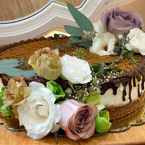 A Bonjour Bakery & Bistro cake with chocolate drizzle, a woven caramel top, and fresh flowers.