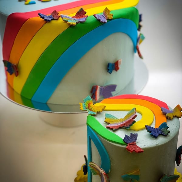 Two tiered cakes with rainbow and butterfly decorations, from Bonjour Bakery & Bistro.