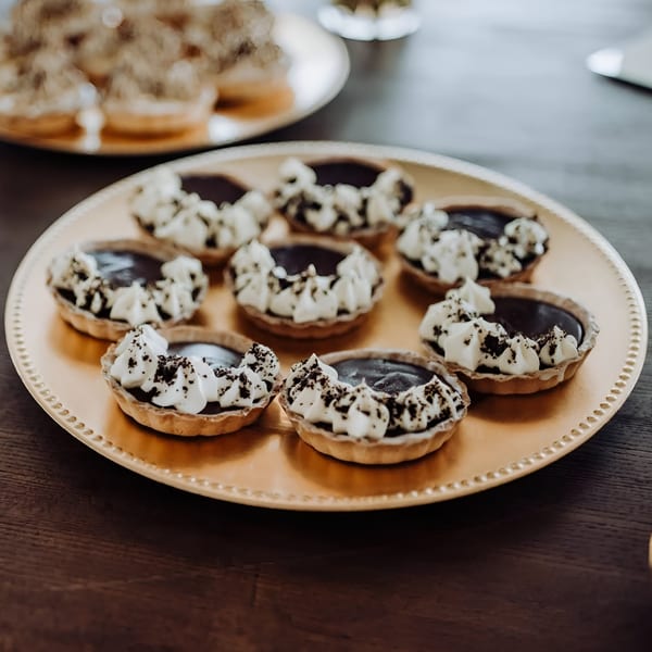 Bonjour Bakery & Bistro's chocolate tarts with whipped cream and cookie crumbles on a gold platter.