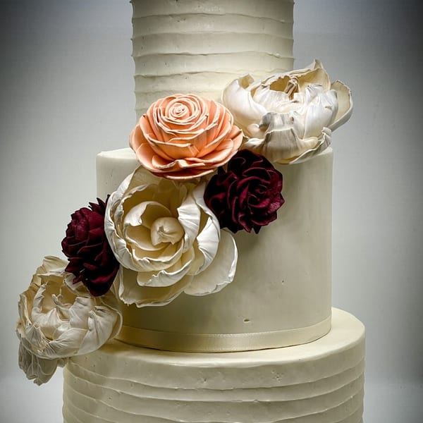 Tiered white wedding cake with peach, cream, and burgundy floral decorations from Bonjour Bakery & Bistro.