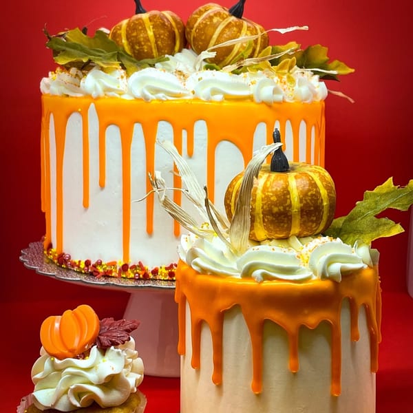 Two pumpkin-decorated cakes with orange drip icing and a matching cupcake on a red background.