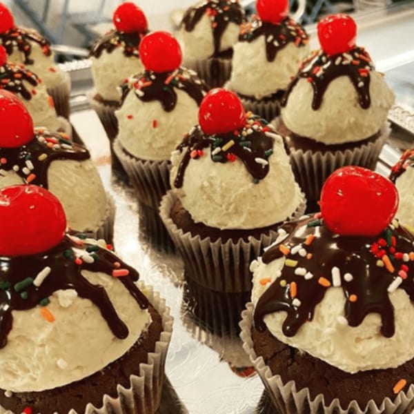 Chocolate cupcakes with white frosting, chocolate drizzle, sprinkles, and a cherry on top.
