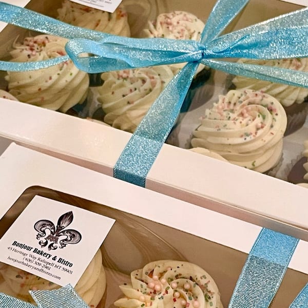 Bonjour Bakery & Bistro cupcakes with white frosting and sprinkles, tied with a blue ribbon.